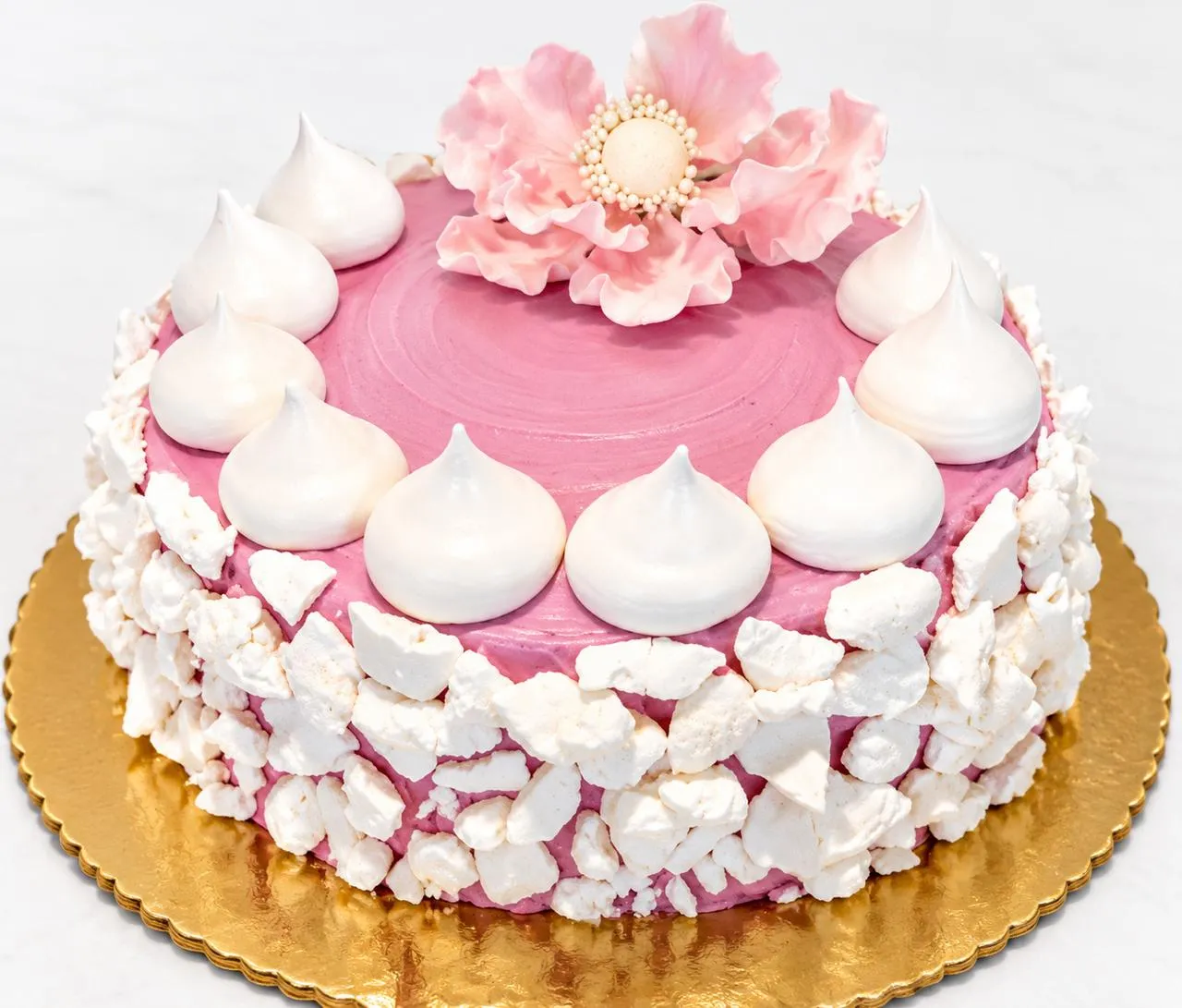Pink meringue cake with a sugar flower on a gold board
