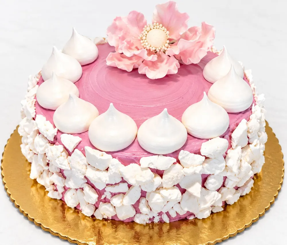 Pink meringue cake with a sugar flower on a gold board